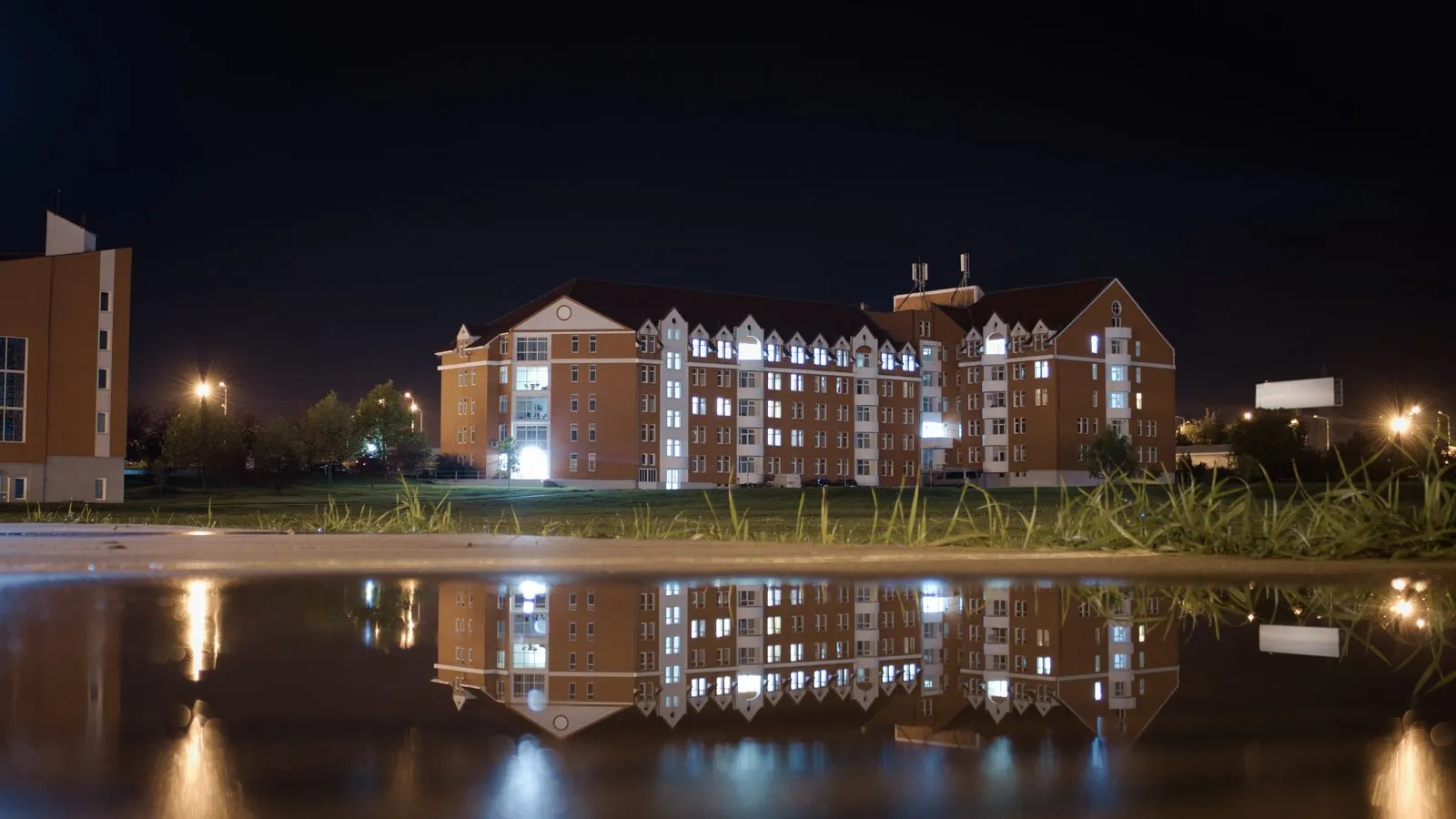 Edificios del campus de la Universidad Emanuel de Oradea (Rumanía), de noche y reflejados en el agua (foto de 2022)