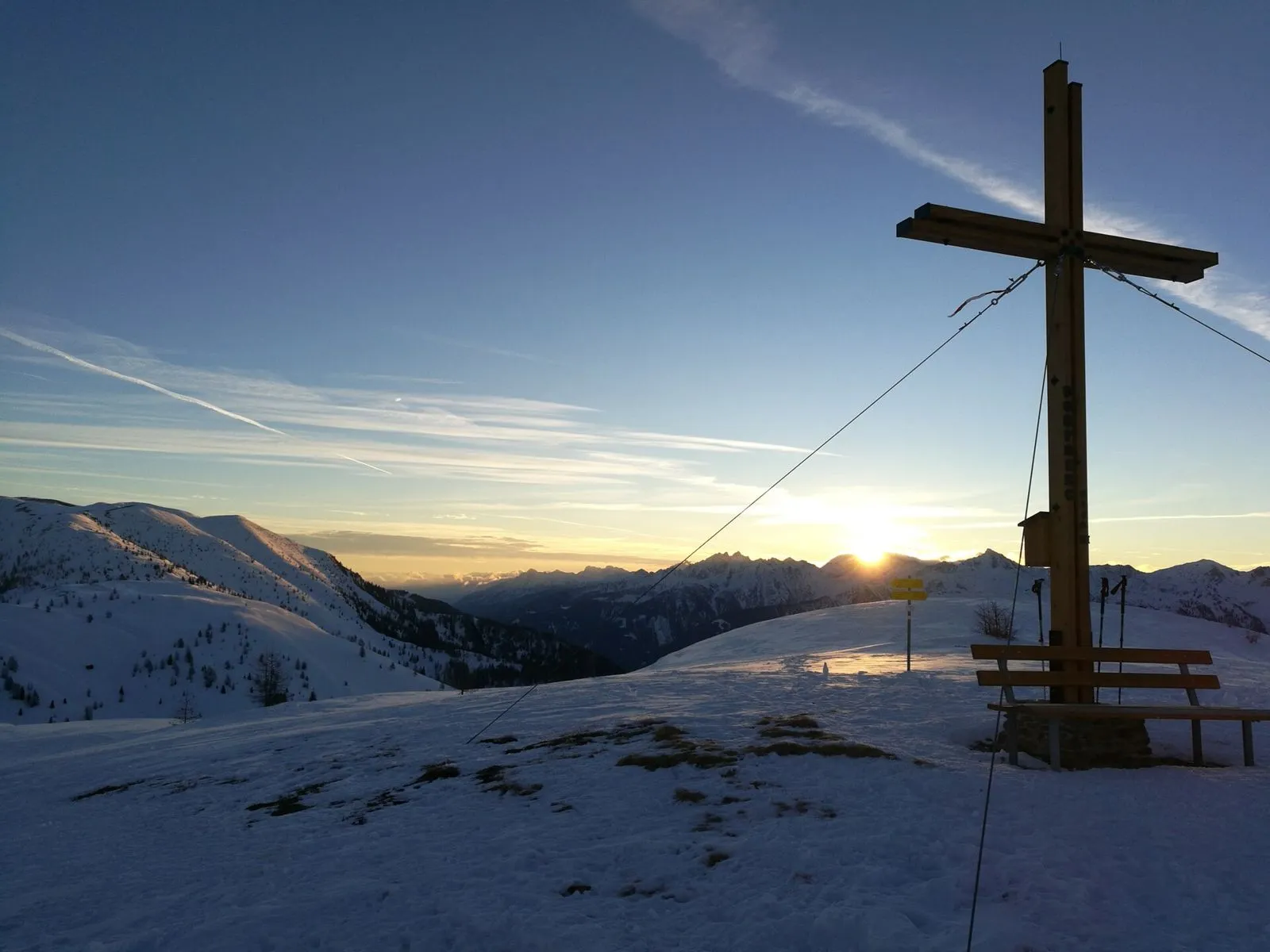 Cruz de madera en la cima de una montaña nevada al amanecer